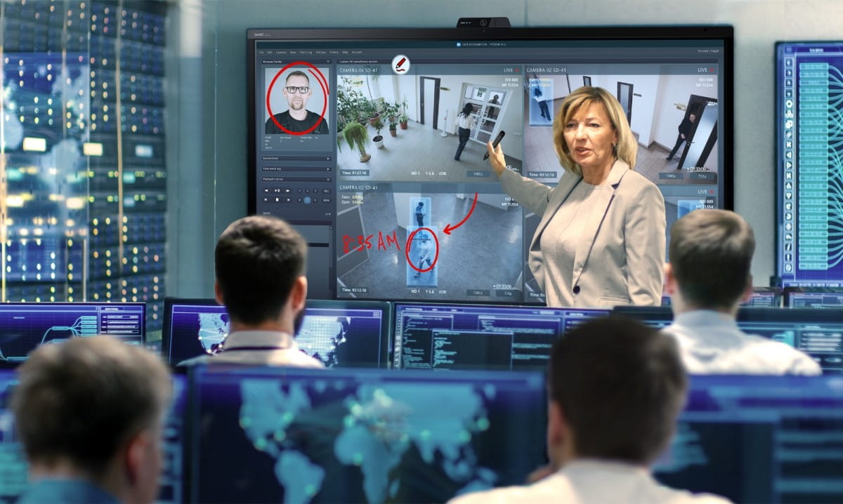 A female officer explains details on a SMART interactive display to her team in a high-tech operations center, pointing at key surveillance images.
