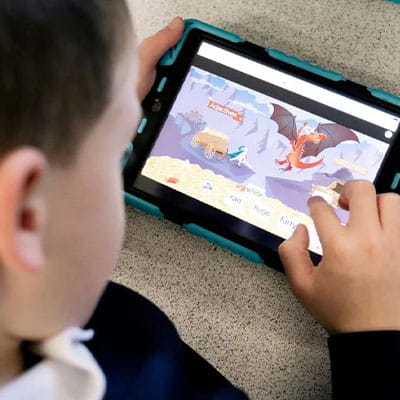 A young student engages with a Lumio educational software on a tablet, arranging adjectives to match with animated animals on the screen.