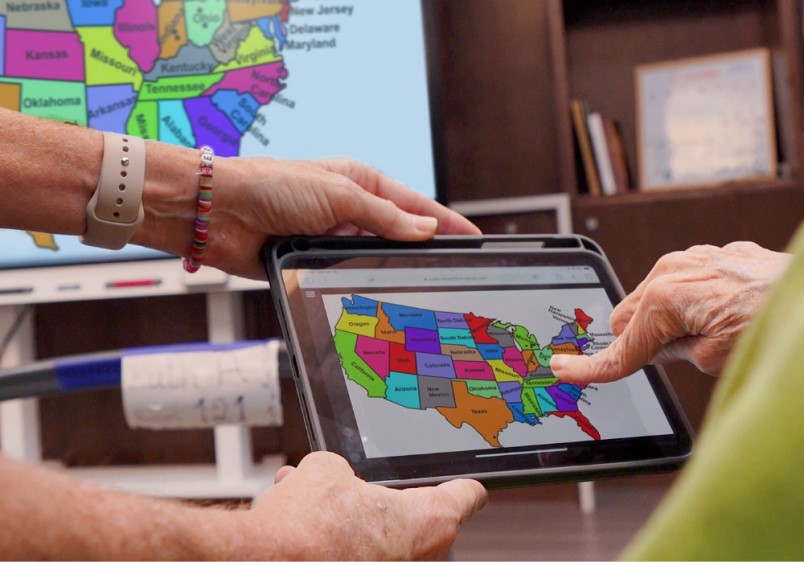 Care home resident hands holding a tablet with a colorful map, indicative of personal learning devices.