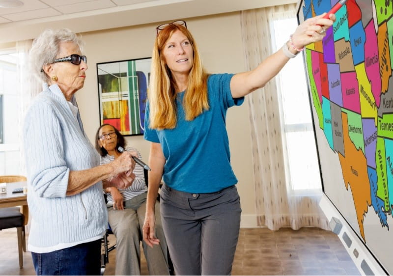 Senior care resident with a  facilitator interacting with a large interactive SMART Board displaying colorful activity choices.
