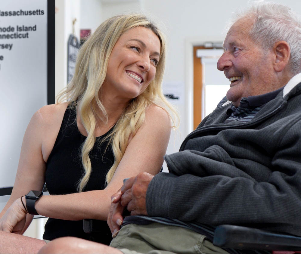 A joyful elderly man in a wheelchair sharing a laugh with a smiling woman in a senior living center.