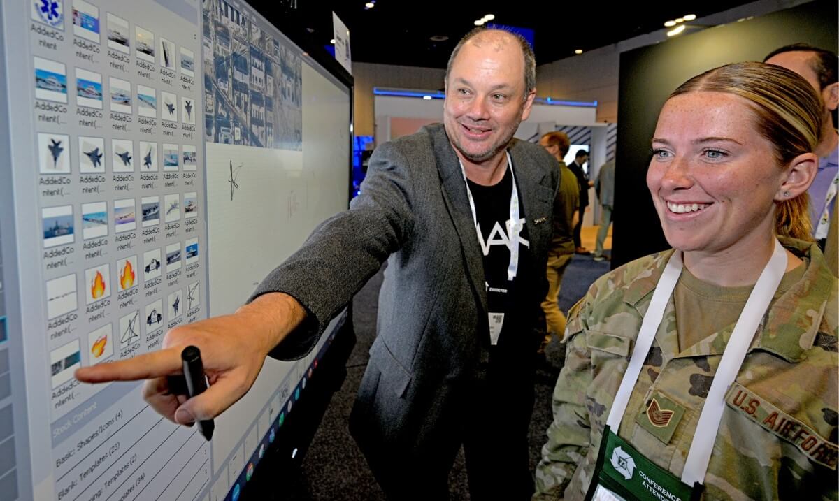 A business professional demonstrates digital content on a SMART interactive display to an engaged military personnel.