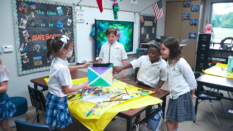 Students in a classroom collaborating on an art project with a SMART Board in the background.