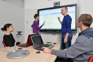 Interactive team meeting with a male presenter using a SMART Board to illustrate points to engaged colleagues in a conference room.